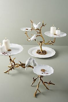 three white plates with birds on them and two candles in the middle one is gold