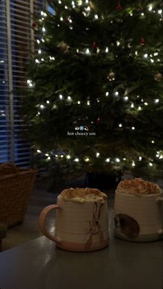 two mugs sitting next to each other in front of a christmas tree