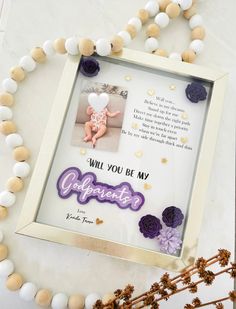 a photo frame sitting on top of a table next to flowers and a beaded necklace