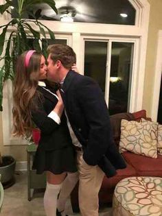 a man and woman are kissing in front of a couch with a potted plant