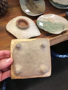 a person holding up a piece of pottery on top of a wooden table next to other plates and bowls