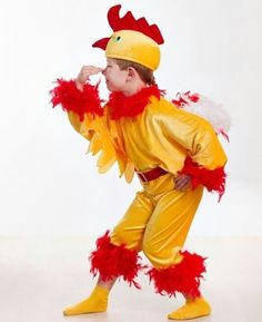 a little boy dressed as a chicken with red feathers on his head and tail, standing in front of a white background