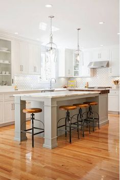 a large kitchen with white cabinets and wooden floors is pictured in this image, there are stools at the center of the island