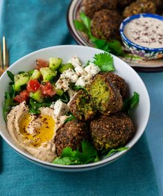 a bowl filled with meatballs and vegetables on top of a blue table cloth next to silverware