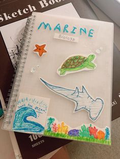 an open notebook with stickers on it sitting next to some books and papers about marine life