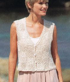 a woman wearing a white top and pink skirt standing in front of water with her hand on her hip