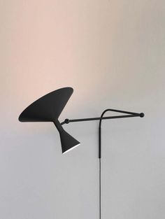 a black lamp on a white wall next to a floor lamp with a long arm