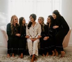 a group of women sitting next to each other on top of a white couch in front of a window