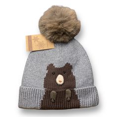 a knitted hat with a brown bear on it and a tag hanging from the front