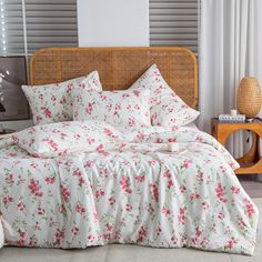 a bed with white and pink flowers on it in front of a wicker headboard