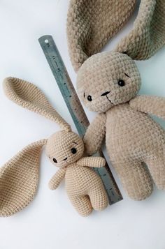 two stuffed animals sitting next to a ruler on a white surface, one is brown and the other is beige