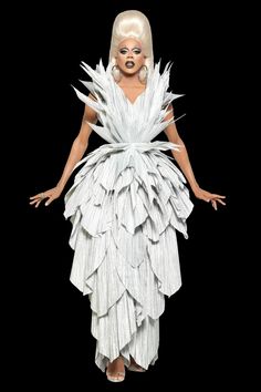 a woman with white hair wearing a dress made out of paper strips and feathers on her body