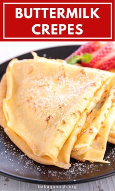 buttermilk crepes on a black plate with strawberries in the background