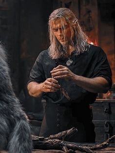 a man with long hair standing in front of a fire