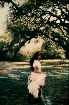 a woman in a white dress is walking through the grass under a large oak tree