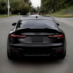 the rear end of a black car parked in front of a tree lined street on a cloudy day