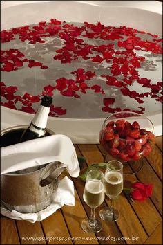 two glasses of champagne and strawberries in a bathtub with rose petals on the floor