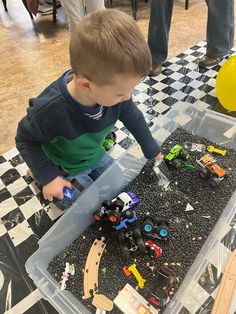 a young boy playing with toy cars in a plastic container on a checkered table