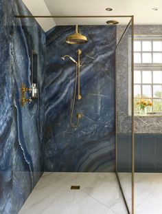 a bathroom with blue marble walls and flooring, gold shower faucet in the corner