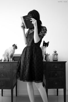 a woman standing in front of a table with two cats on it and holding a book