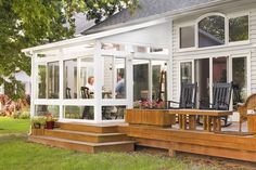 a white house with wooden steps leading up to the front porch and patio area that has chairs on it