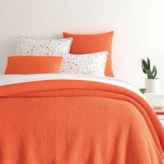 an orange comforter and pillows in a white room with potted plants on the side