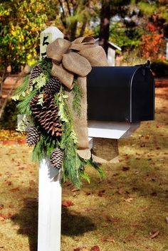 a mailbox decorated with pine cones, evergreens and burlap bow tied to it