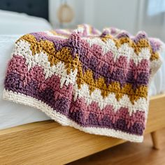 a crocheted blanket laying on top of a bed next to a night stand