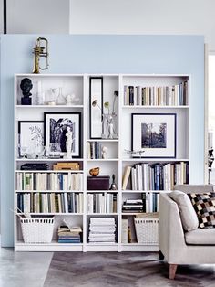 a living room filled with lots of books on top of a white book shelf next to a couch