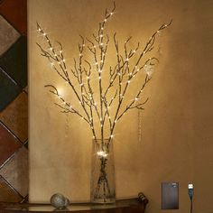 a vase filled with branches sitting on top of a wooden table next to a phone charger