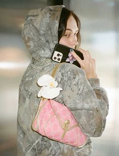 a woman in camouflage carrying a pink purse and looking at her cell phone while wearing a hoodie