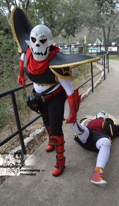 two people dressed in costumes and one is laying on the ground next to a fence