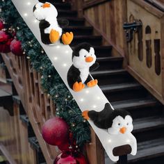 three stuffed penguins sitting on top of a white rail next to christmas decorations and stairs