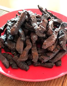 a red plate topped with beef strips on top of a wooden table