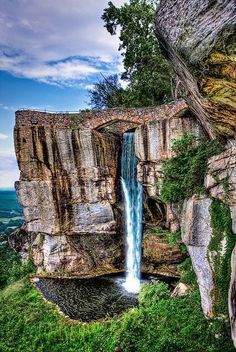 an image of a waterfall coming out of the side of a rock cliff with grass and trees around it