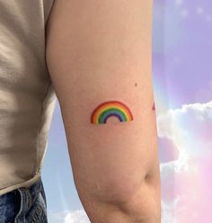 a person with a rainbow tattoo on their arm and the sky in the back ground