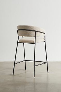 an upholstered chair sits in front of a plain white wall and concrete floor