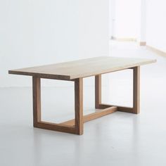 a wooden table sitting on top of a white floor next to a window in an empty room