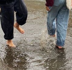 two people are walking in the water with their feet up and one person is holding an umbrella