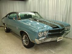 a blue car parked in a garage next to a white wall and curtained area