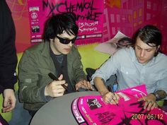 two young men sitting at a table signing autographs for someone to sign on them