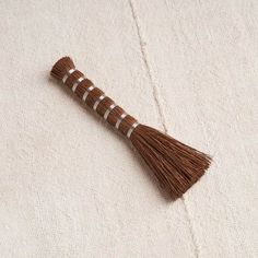 a brown and white tasseled broom laying on top of a beige cloth covered surface