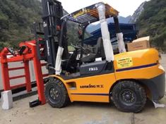 a yellow forklift parked next to a red gate and some mountains in the background