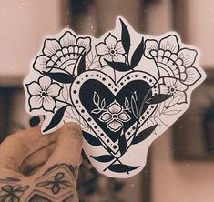 a person holding up a heart shaped sticker with flowers and leaves on it's side