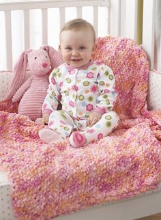 a baby is sitting in a crib with a pink blanket and stuffed animals on the bed