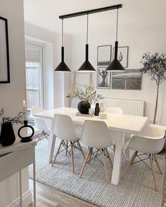 a dining room table with white chairs and black pendant lights