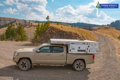 a truck with a camper attached to the back parked on a dirt road in front of mountains