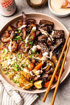 a bowl filled with rice, meat and vegetables next to chopsticks on a table