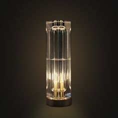 a clear glass table lamp sitting on top of a black surface with dim lights in the middle