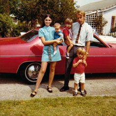 a family poses in front of a red car